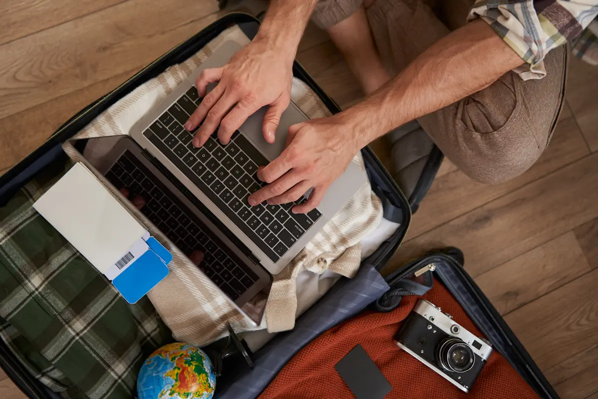 Un homme sur un ordinateur posé sur une valise pleine